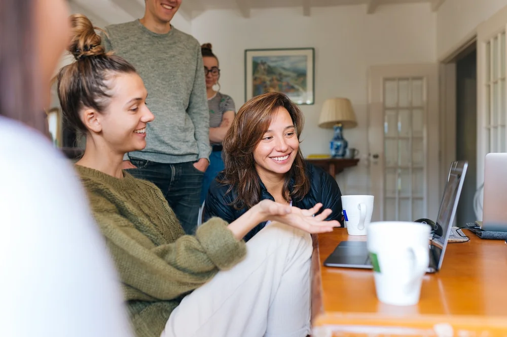 Young people sitting and standing in front of a laptop