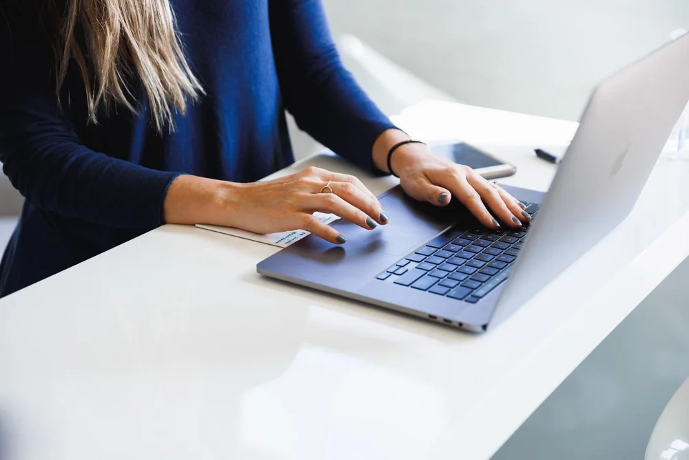 A woman typing on a laptop. Her royal-blue nails match her top.