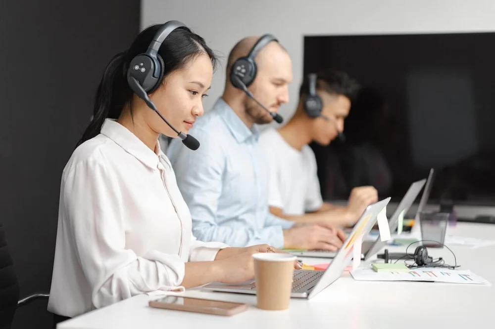 Three people wearing headsets, working on their laptops. They look like customer service reps