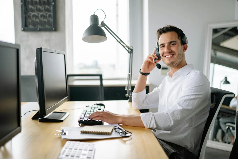A man sitting in an office wearing headphones while smiling