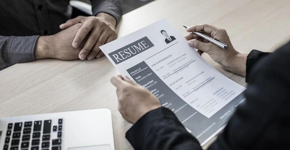 An interviewer is reading a resume while sitting across from a candidate. Both their faces and torsos are offscreen.