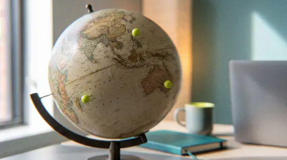 Vintage-style world globe with lime-green map pins on a modern office desk, symbolizing Somewhere's global offshore direct hire recruitment across international talent markets