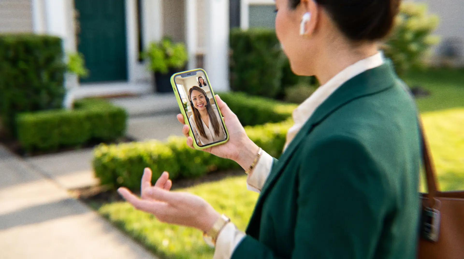 Real estate broker on a video call with her offshore real estate virtual assistant outside a suburban home