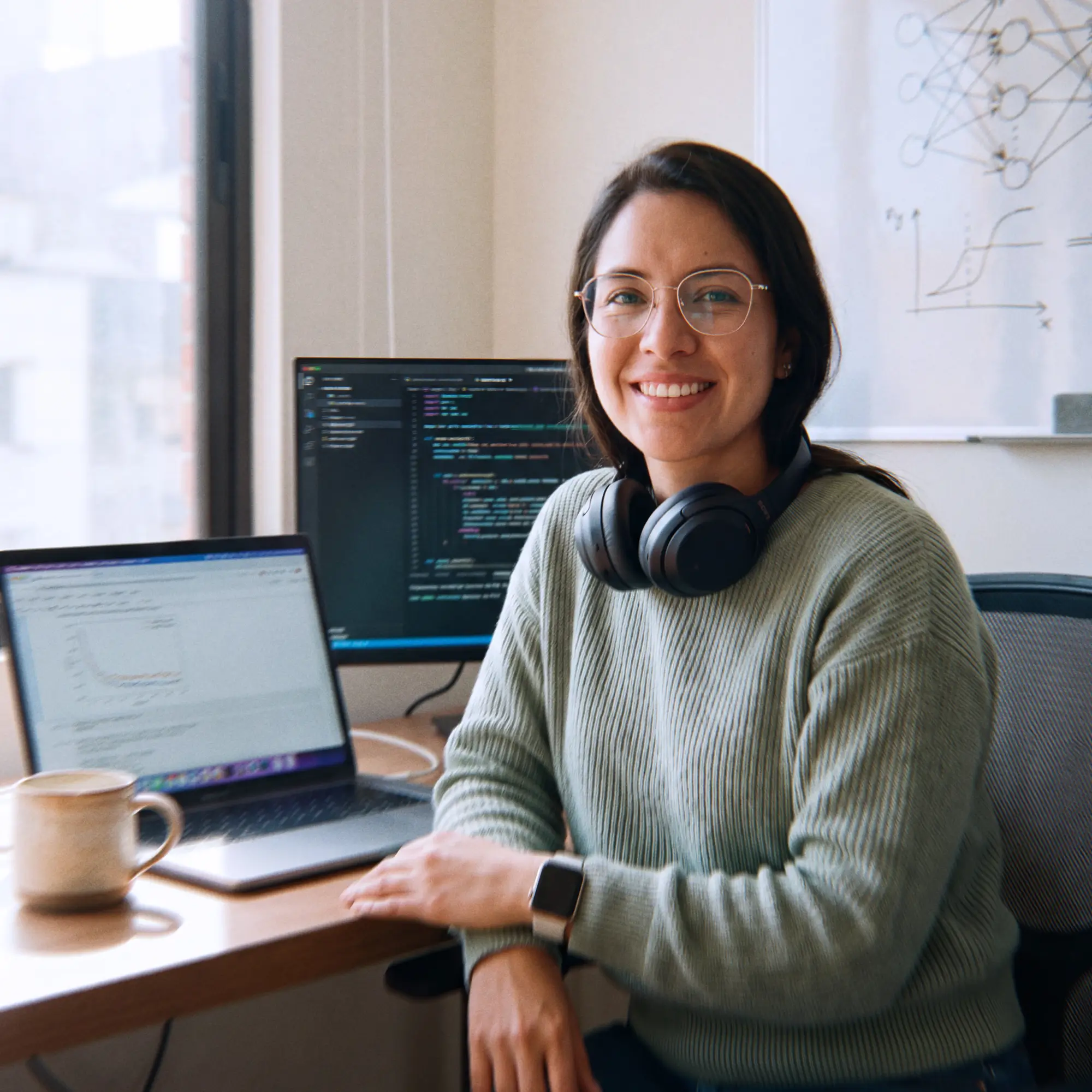 Colombian machine learning engineer smiling at her home-office desk beside a laptop showing a model training chart