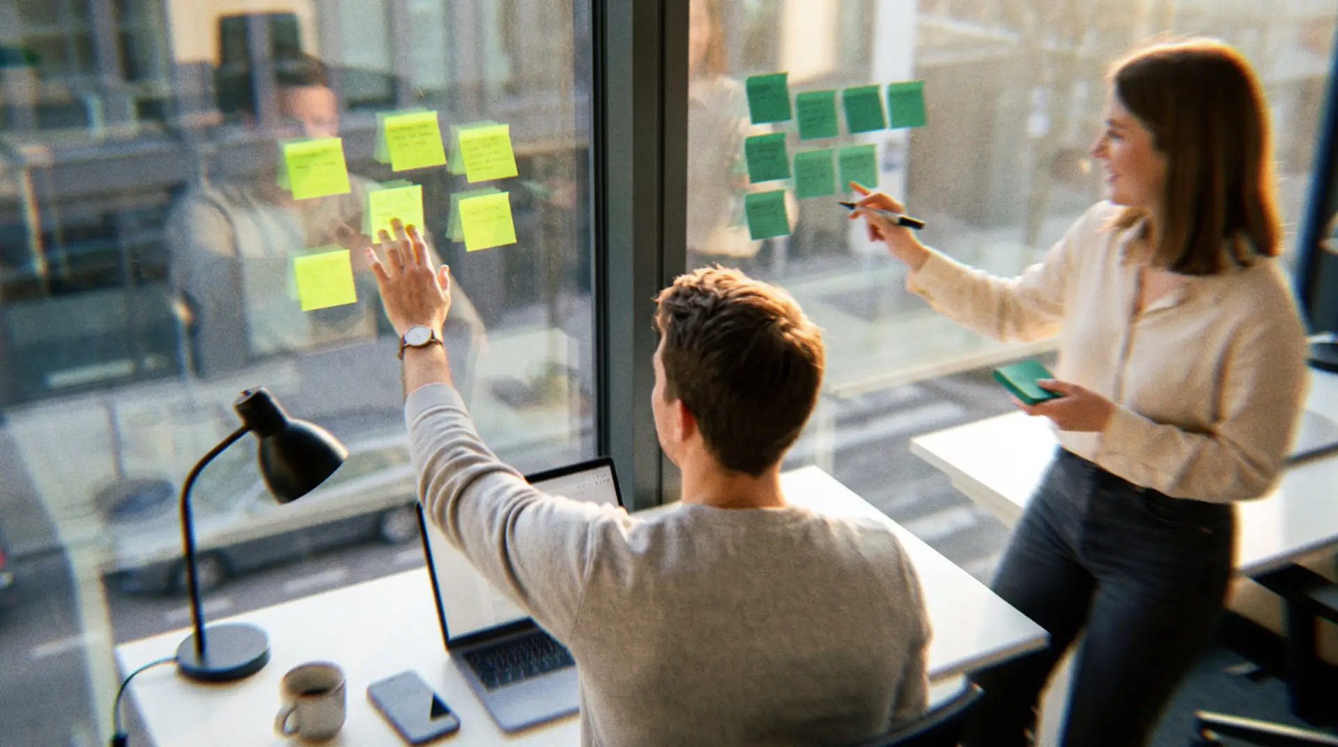Founder and operations manager sorting sticky notes on an office window to decide which roles can be outsourced to remote international employees, by function