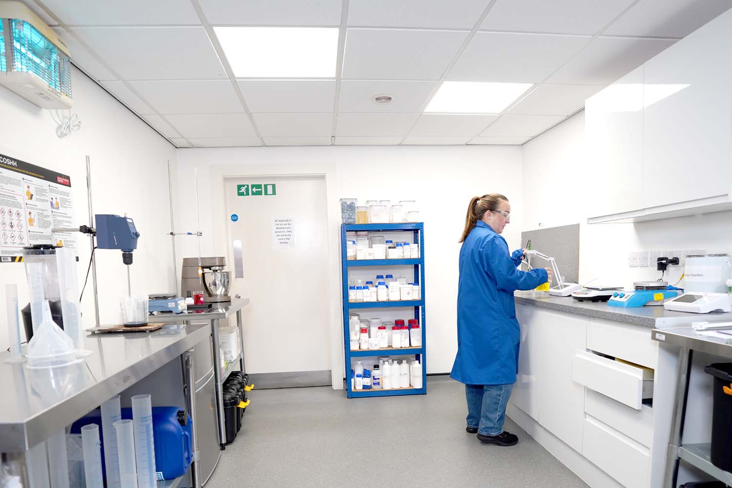 Person in blue lab coat working with lab equipment on a countertop inside a clean laboratory.