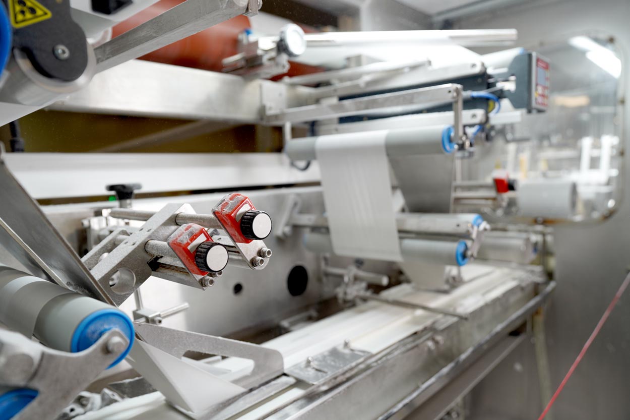 Close-up of industrial packaging machine processing and sealing plastic films on rollers.