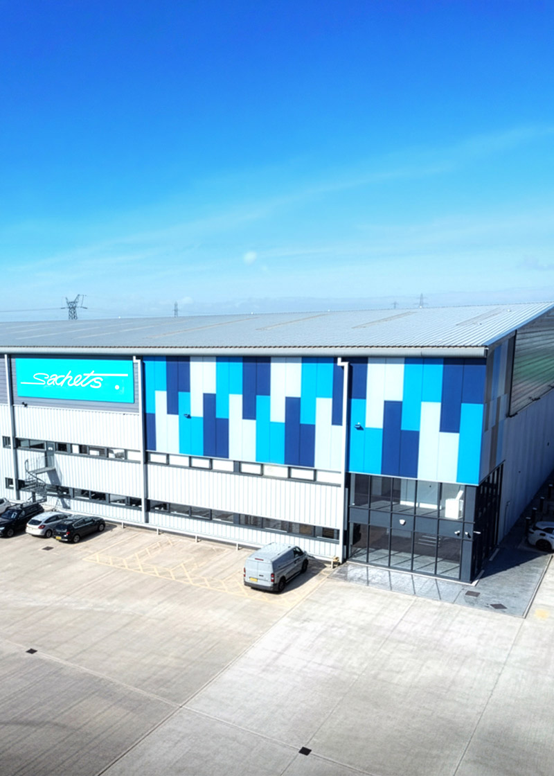 Modern industrial building with blue and white vertical panels and a sign reading 'Sachets' under a clear blue sky.