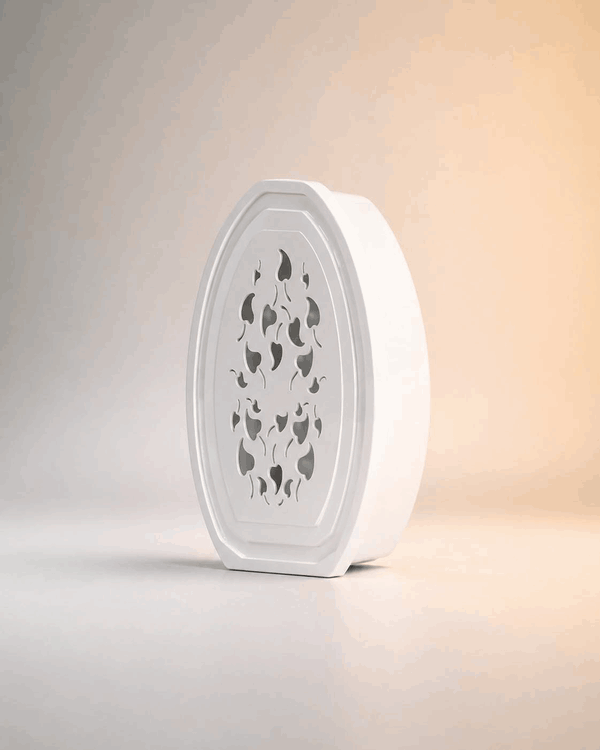 White decorative gel air freshener with flame-shaped cutouts on the front panel, rotating slowly on a neutral background.