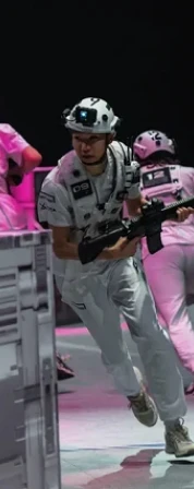 Person in white tactical gear and helmet holding a rifle, running indoors during a game or simulation with others in similar gear.