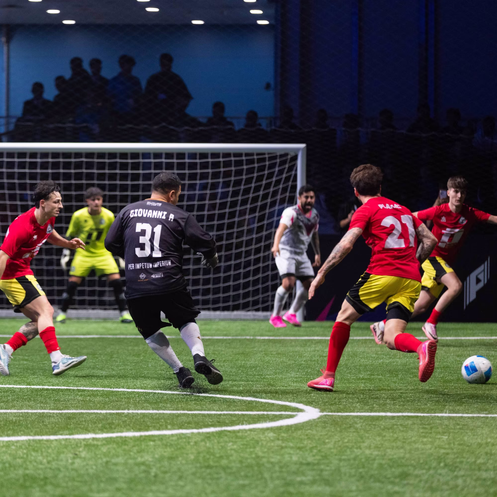 Two esports players in white jerseys focused on their game controllers during a tournament with a large screen displaying the word 'GOAL' behind them.