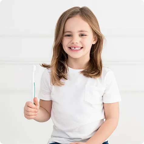 Smiling young girl holding a toothbrush while wearing a white t-shirt.