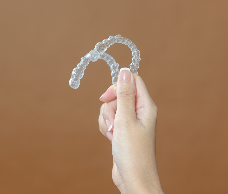 Hand holding two clear dental aligners against a brown background.