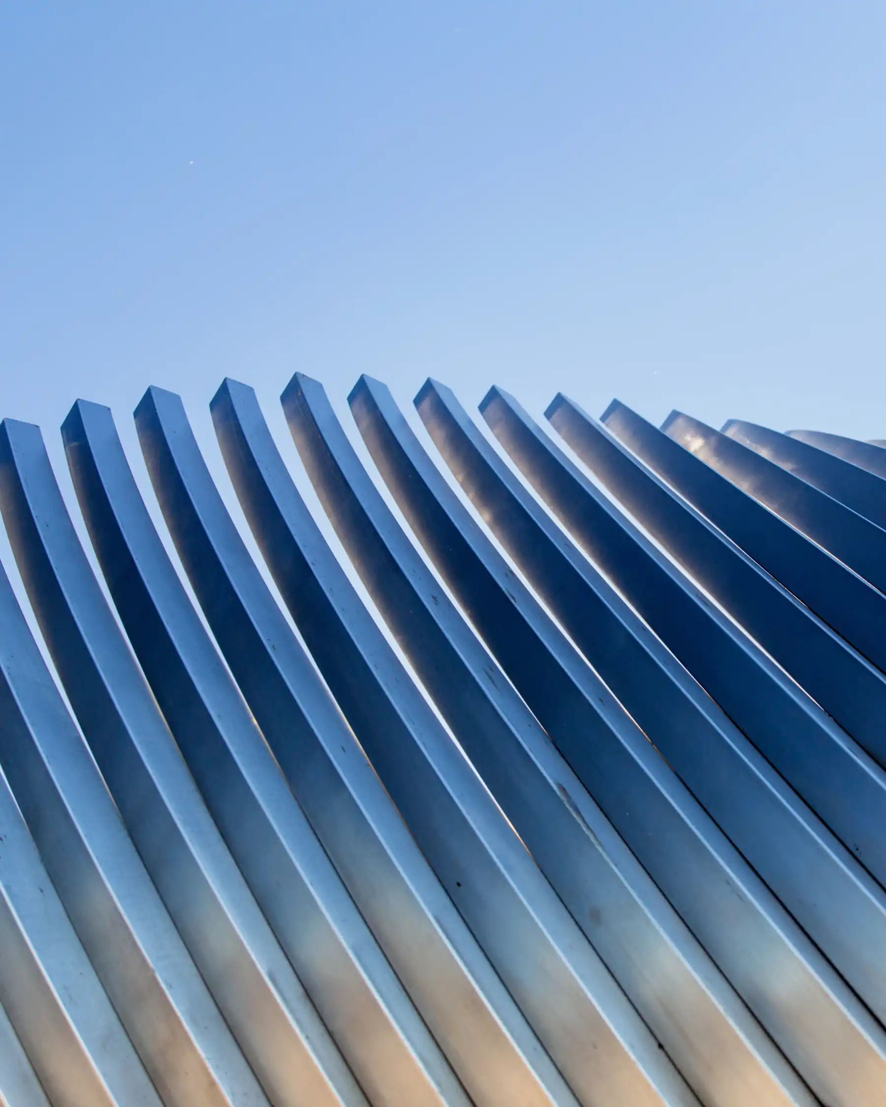 Close-up of curved metallic architectural fins against a clear blue sky.
