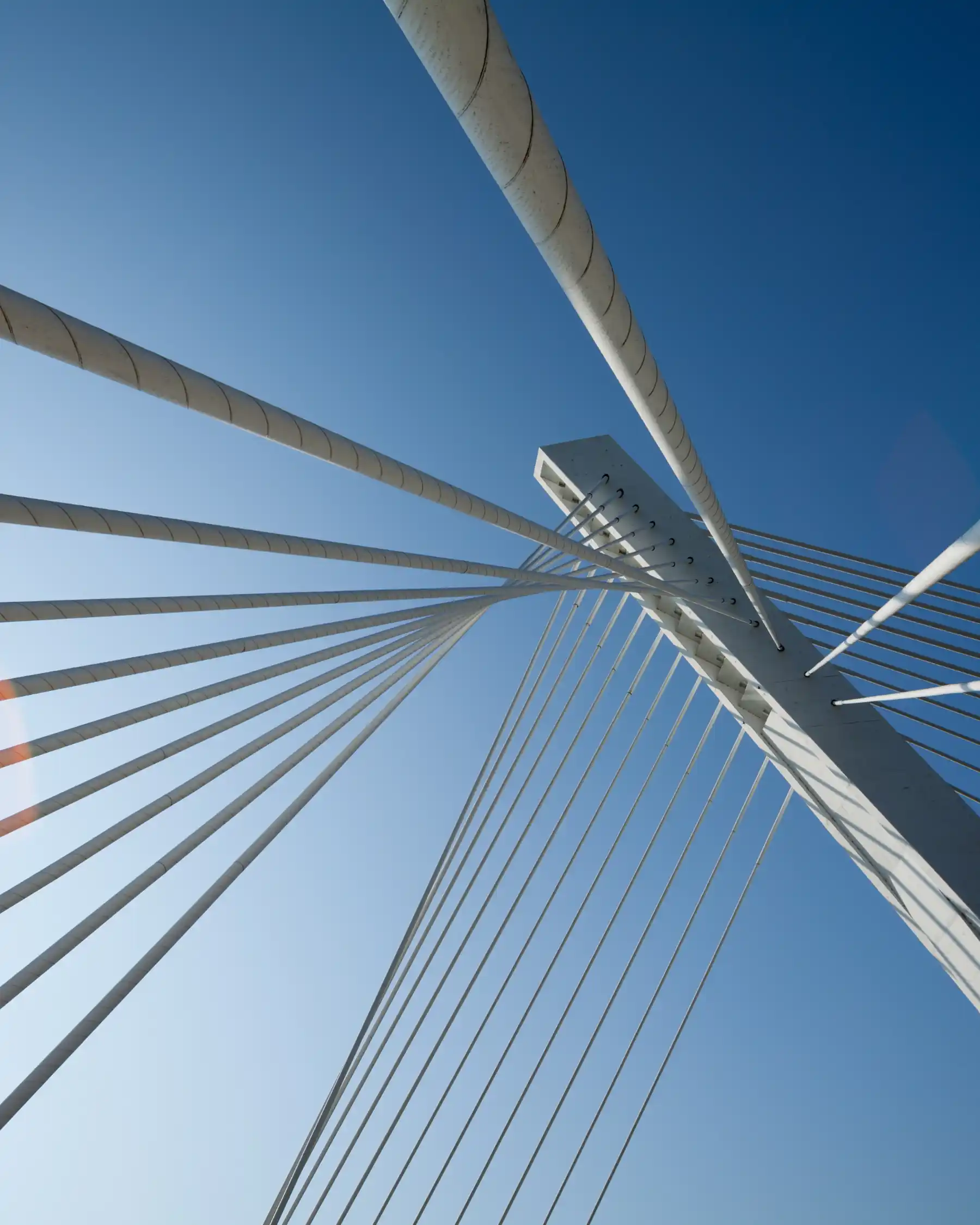 View looking upward at cables and supporting tower of a modern cable-stayed bridge against a clear blue sky.