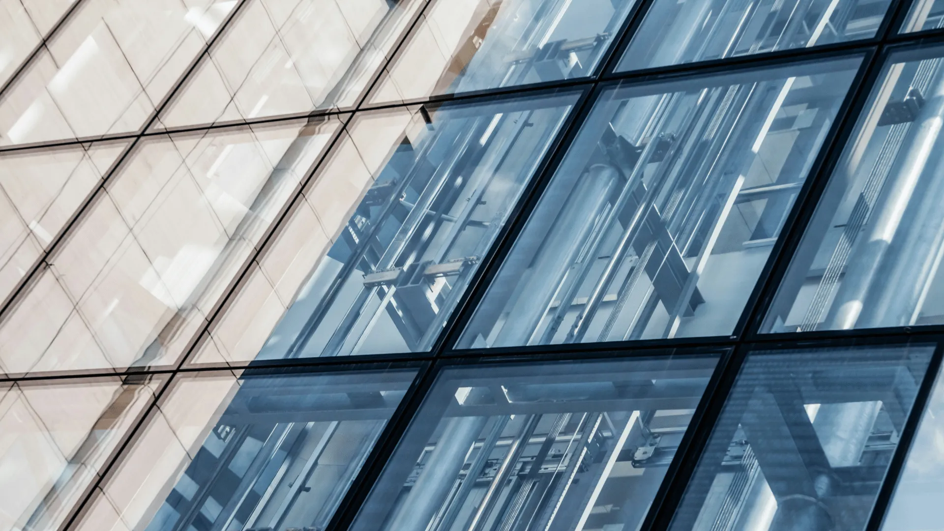 Close-up view of a modern building facade with reflective glass panels showing structural metal beams and pipes inside.