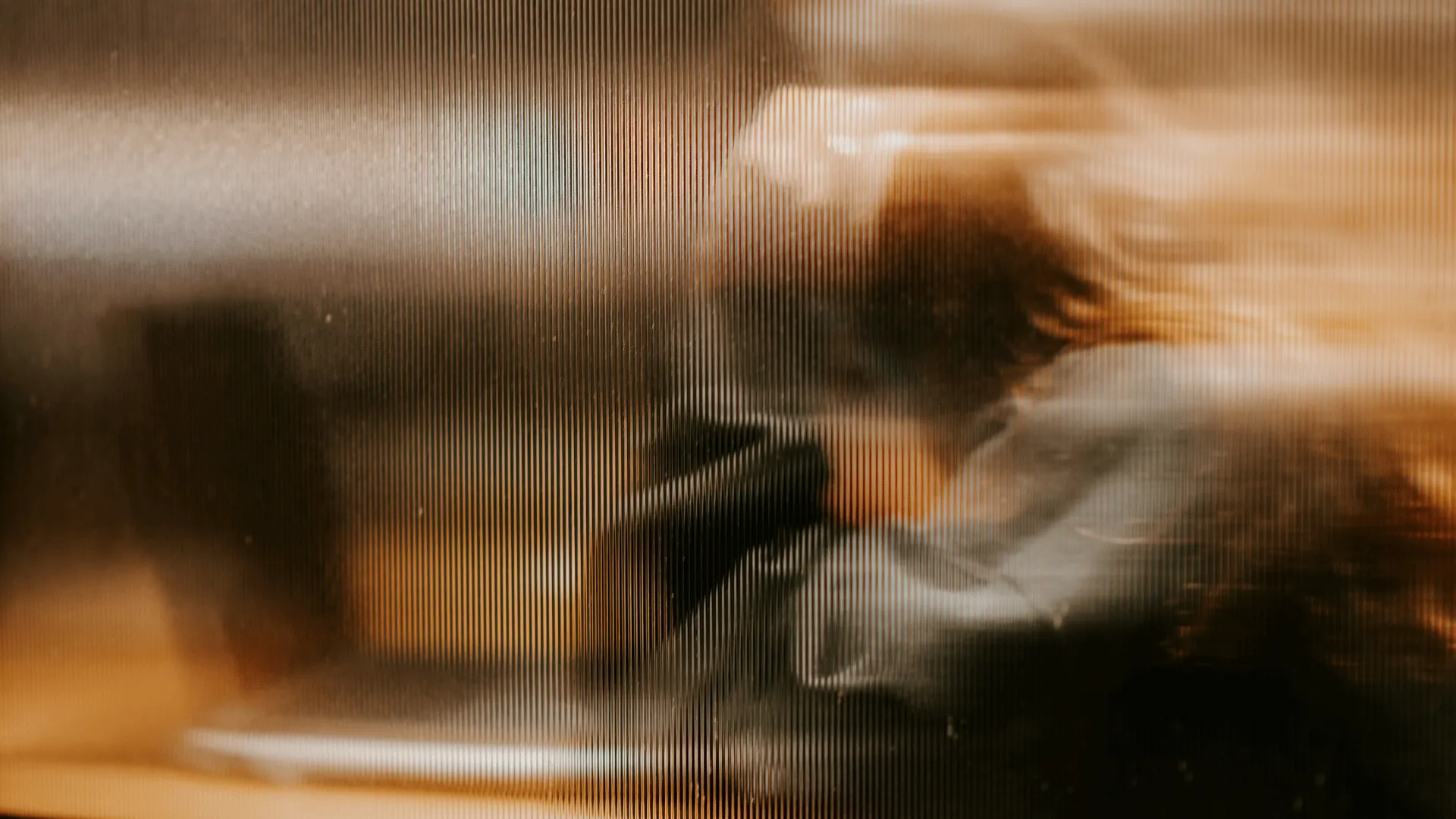 Blurred silhouette of a person with raised hands behind textured glass panel in warm lighting.