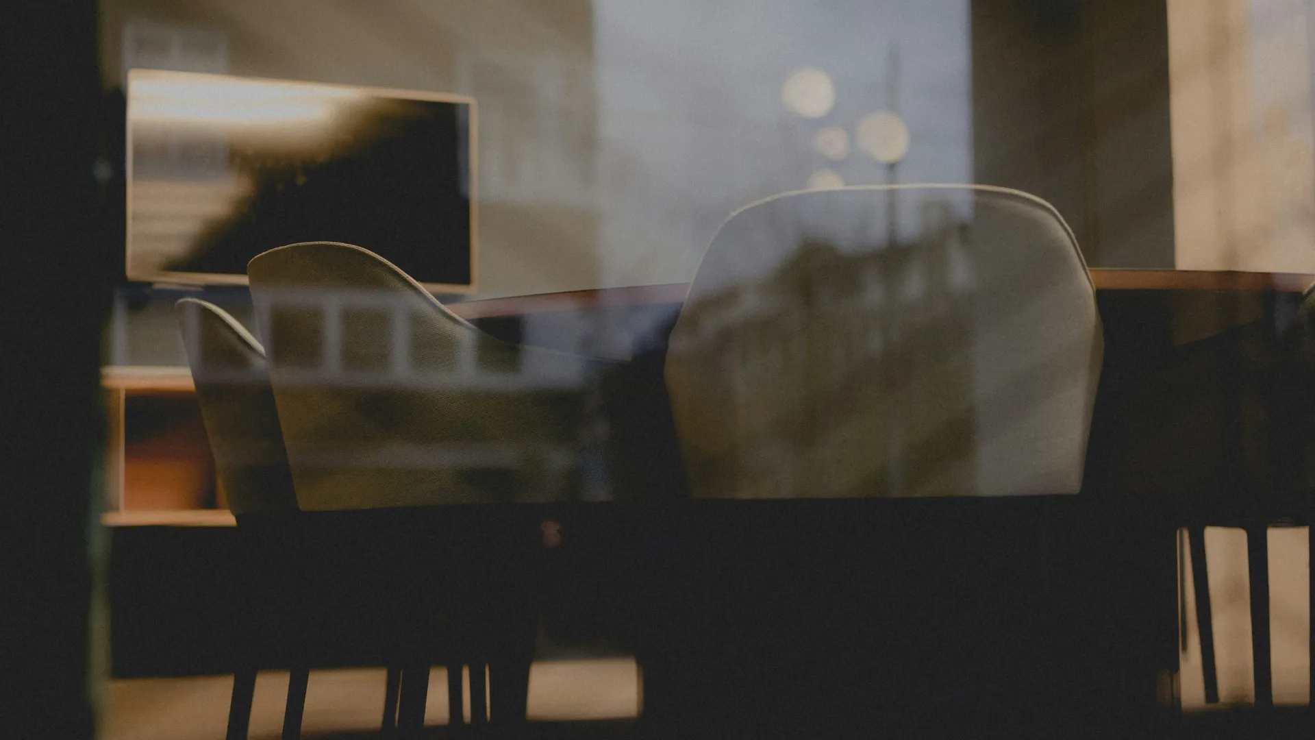 Empty office conference room with chairs around a table and a monitor, seen through a window with reflections.