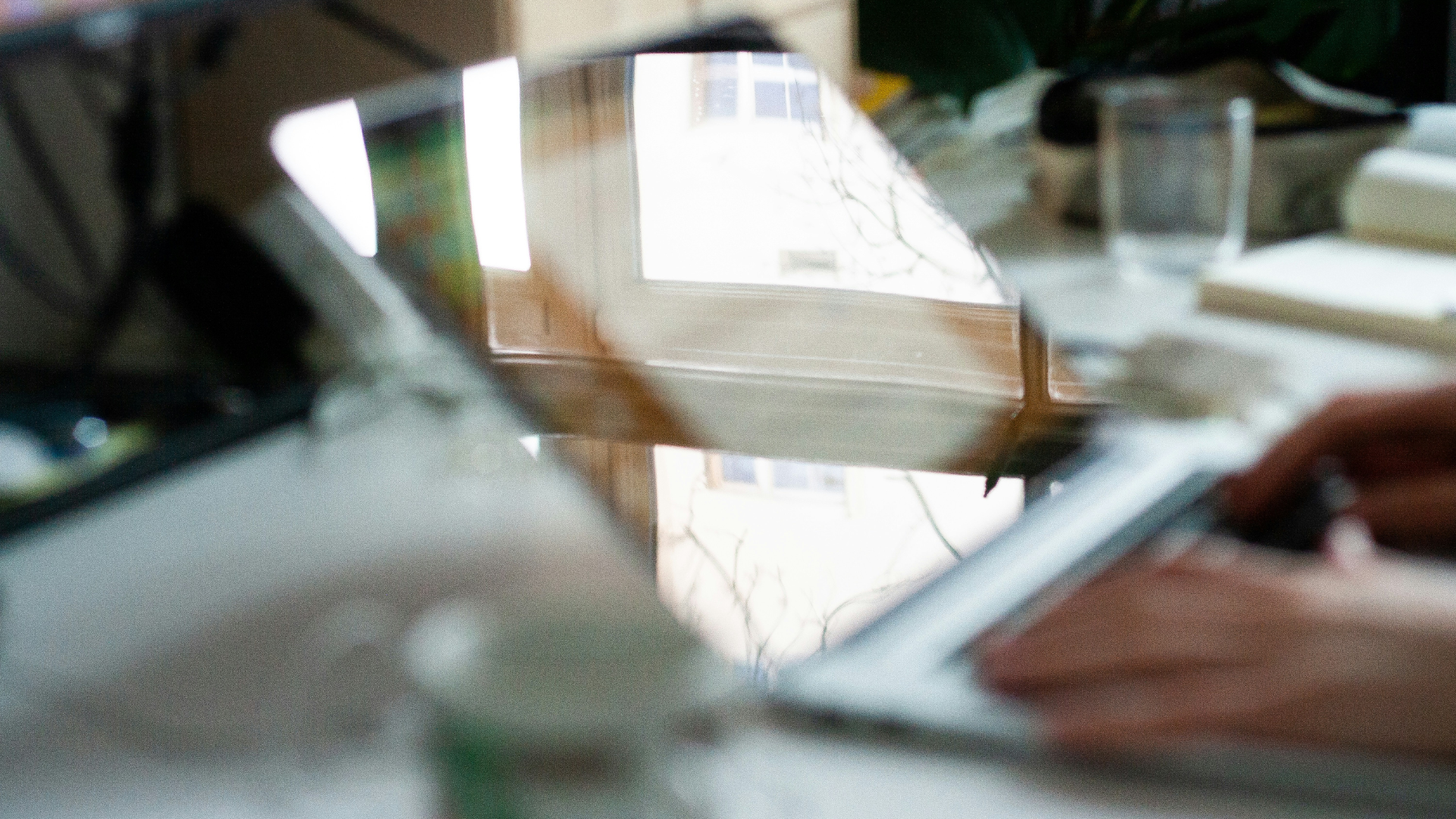 Close-up of hands typing on a laptop keyboard with a window reflection on the screen.