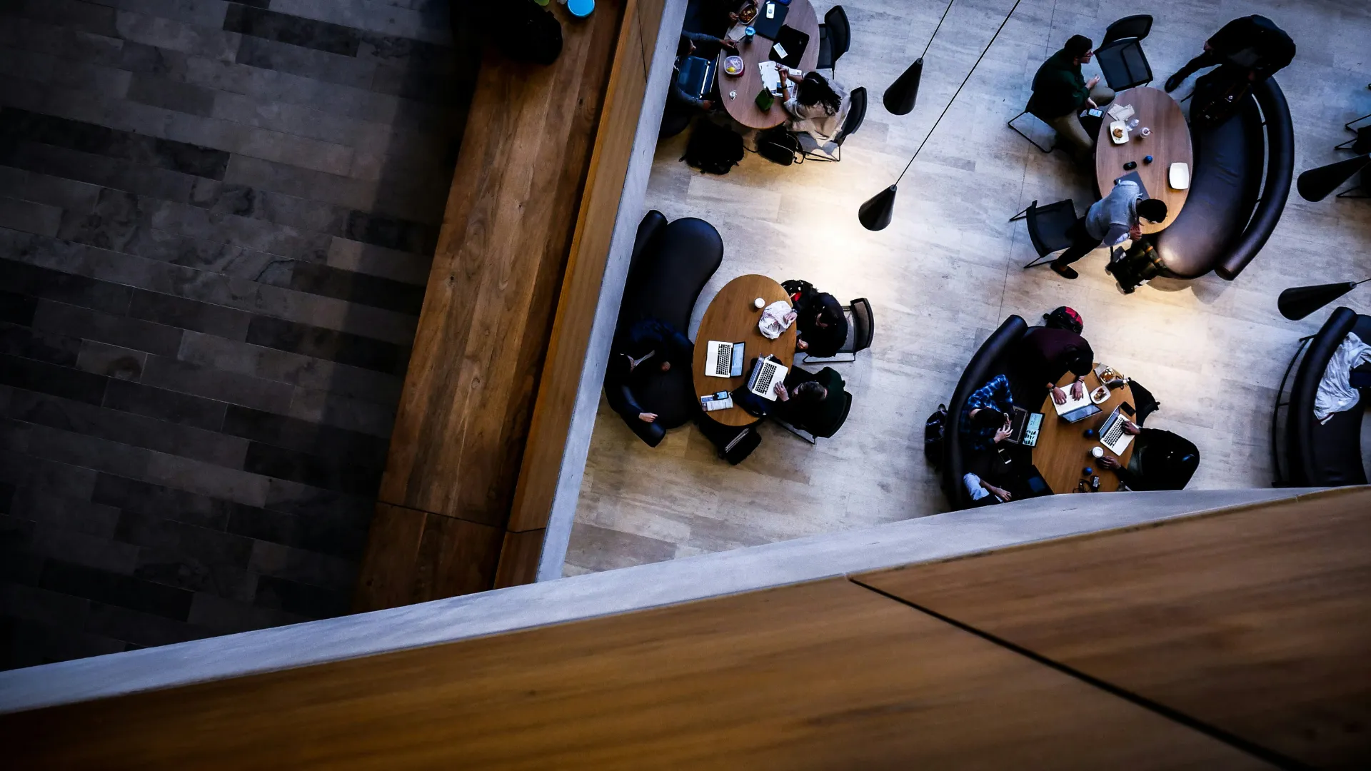 Overhead view of people working and socializing at round tables with laptops and coffee in a modern indoor space.