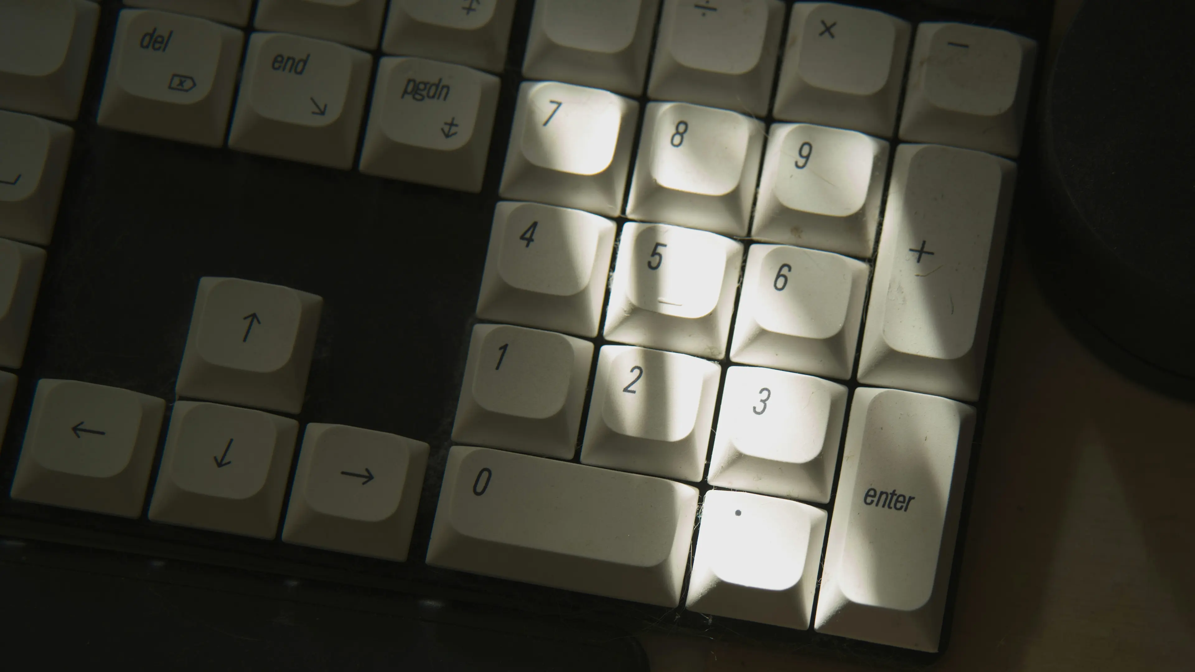 Close-up of a numeric keypad section on a keyboard with white keys illuminated by light.