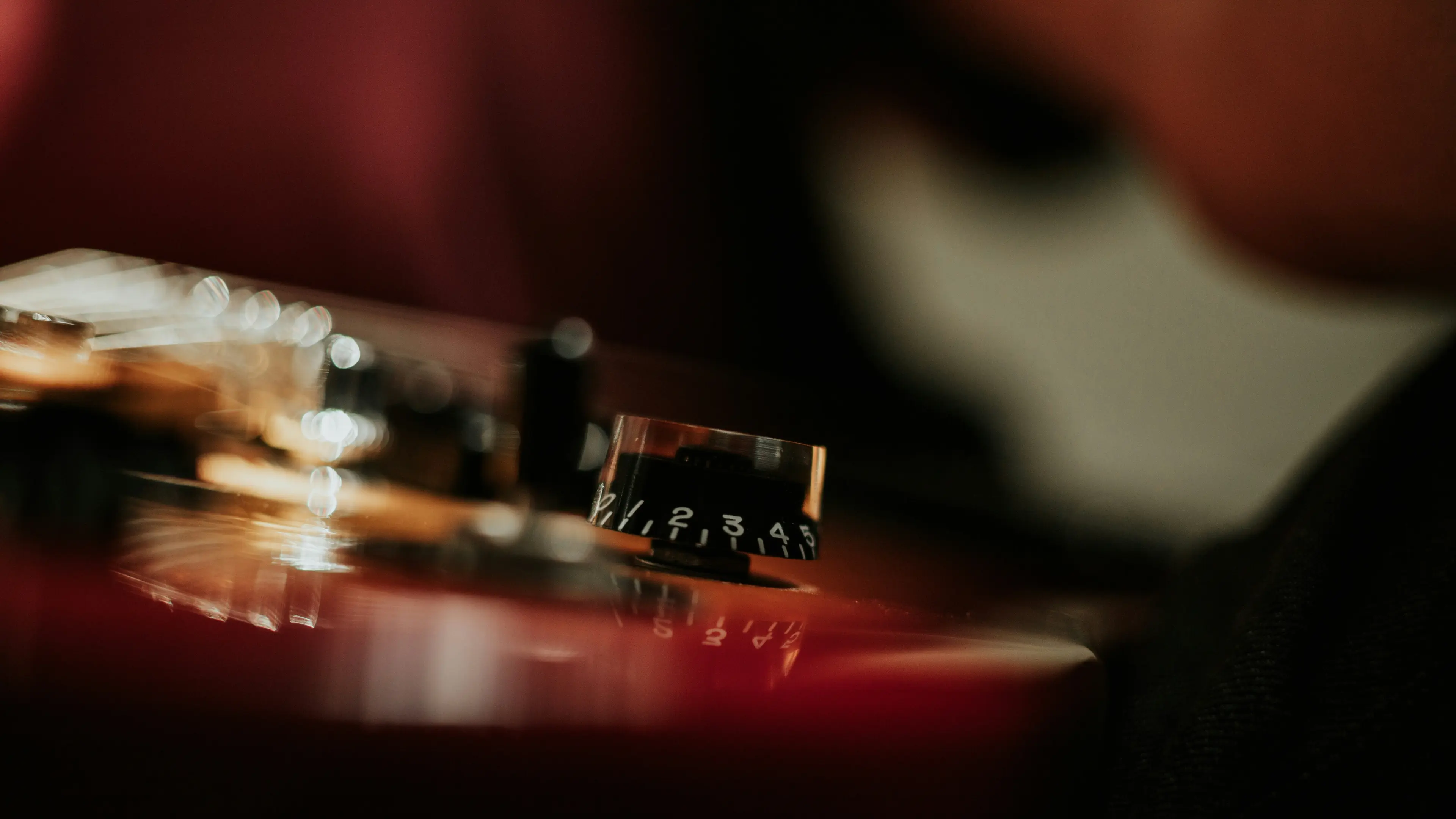Close-up of a guitar volume knob with numbers 1 to 5 in focus on a glossy guitar body.