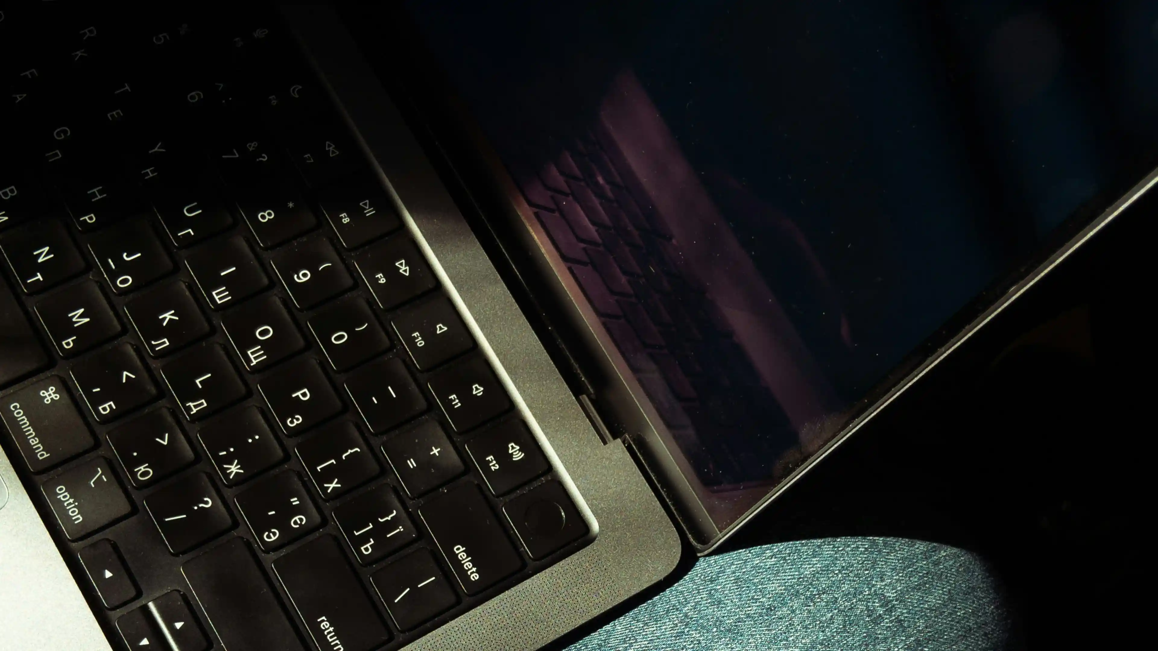Close-up of a laptop keyboard with part of a dark screen reflecting the keyboard.