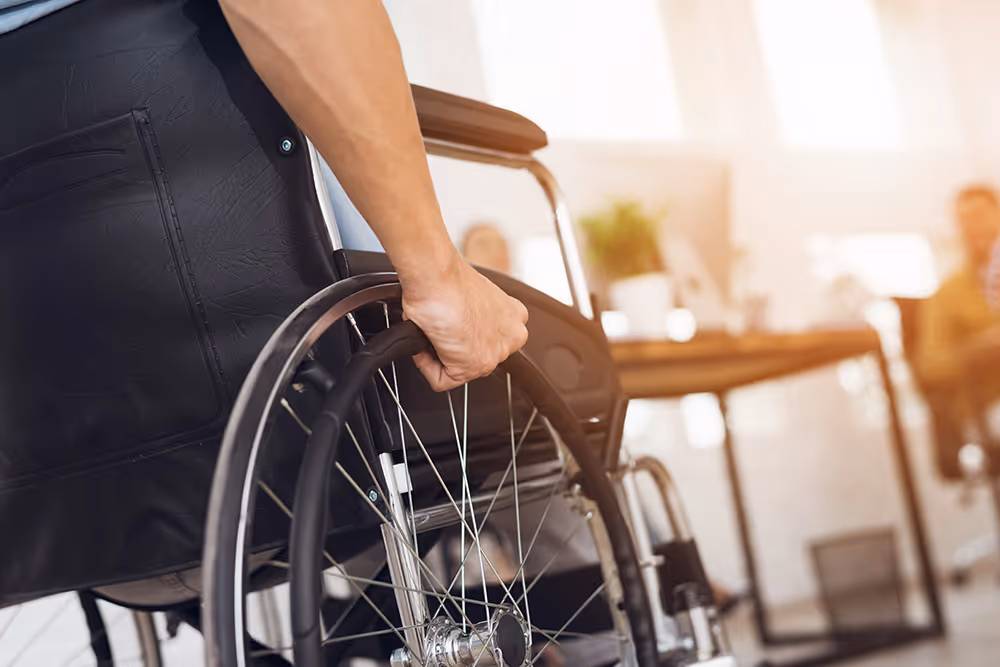 Close-up of a person’s hand gripping the wheel of a wheelchair in a bright office setting.