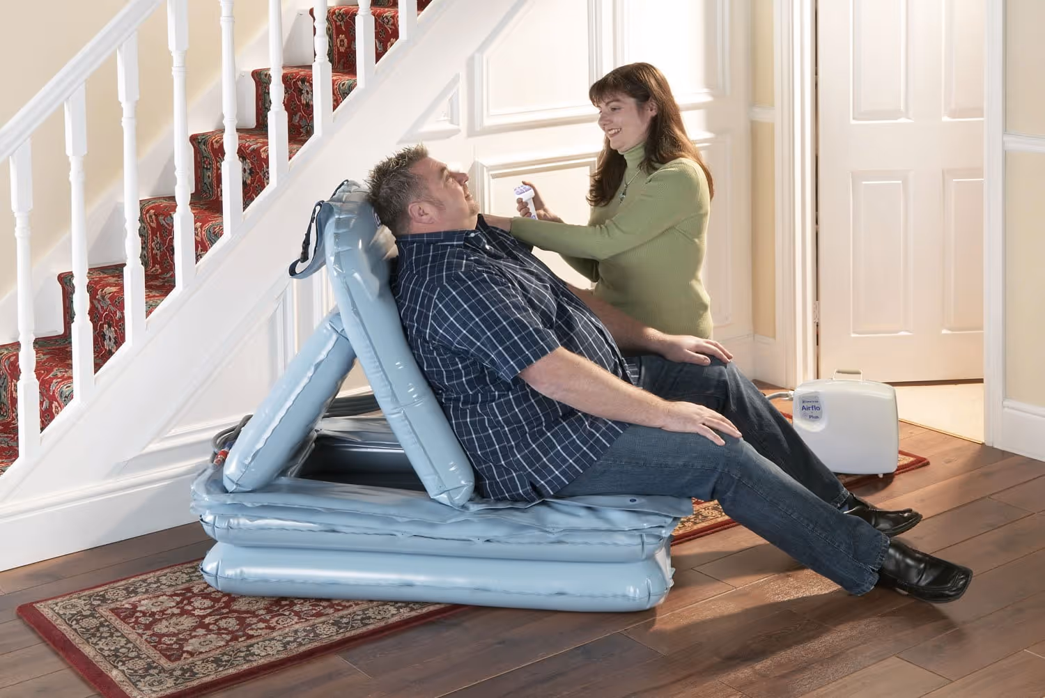 Man sitting on an inflatable chair indoors with a woman holding a remote control and smiling at him.