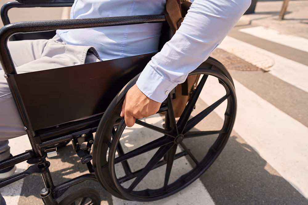 Person in blue shirt manually operating the wheel of a black wheelchair on a crosswalk outdoors.