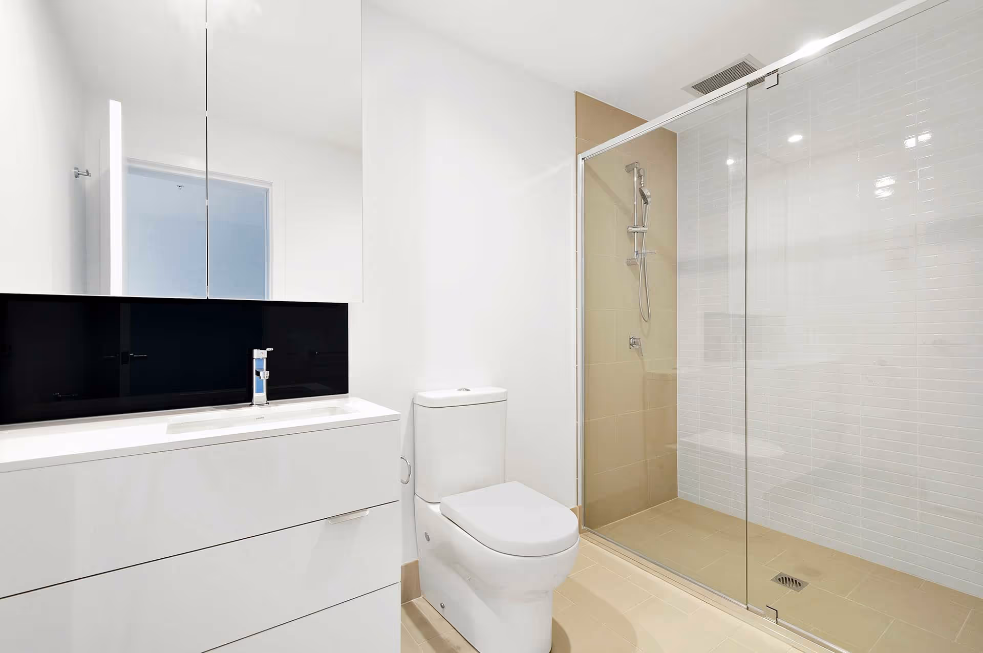 Modern white bathroom with toilet, vanity with black backsplash, and glass shower enclosure.