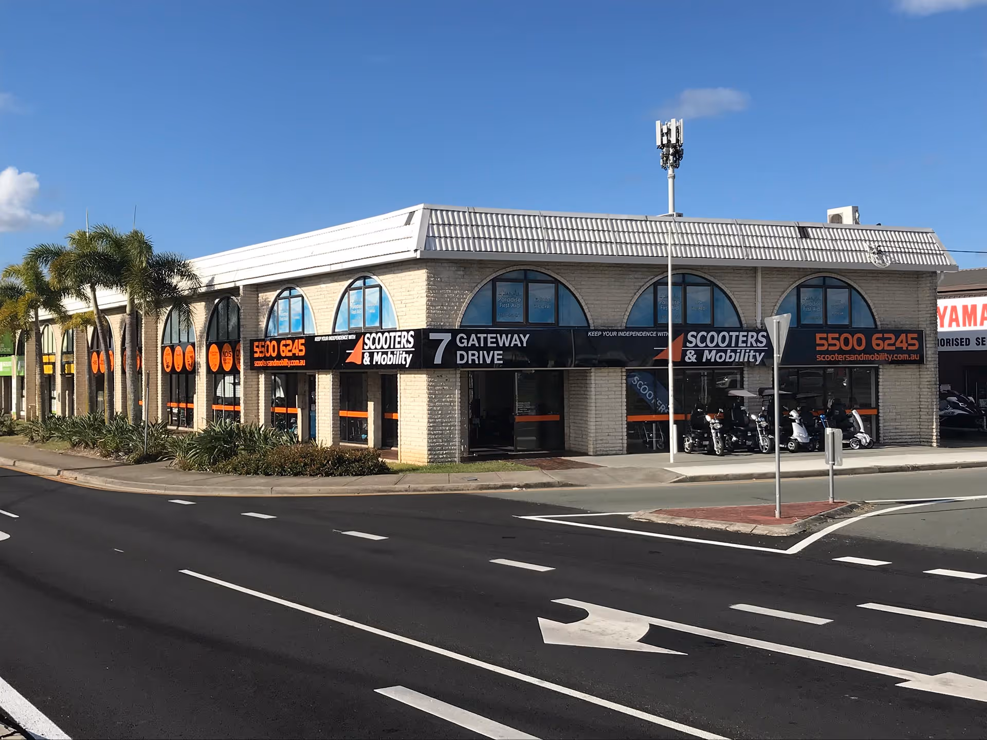 Corner building of Scooters & Mobility at 7 Gateway Drive with palm trees and parked scooters visible.