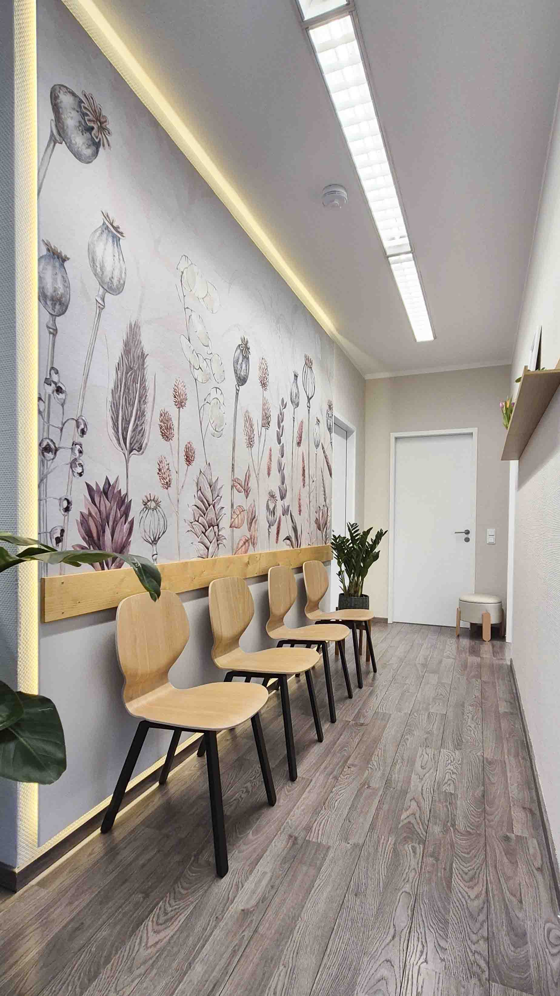 Wartezimmer mit Holzstühlen, einer Wand mit botanischem Muster und Zimmerpflanzen.
