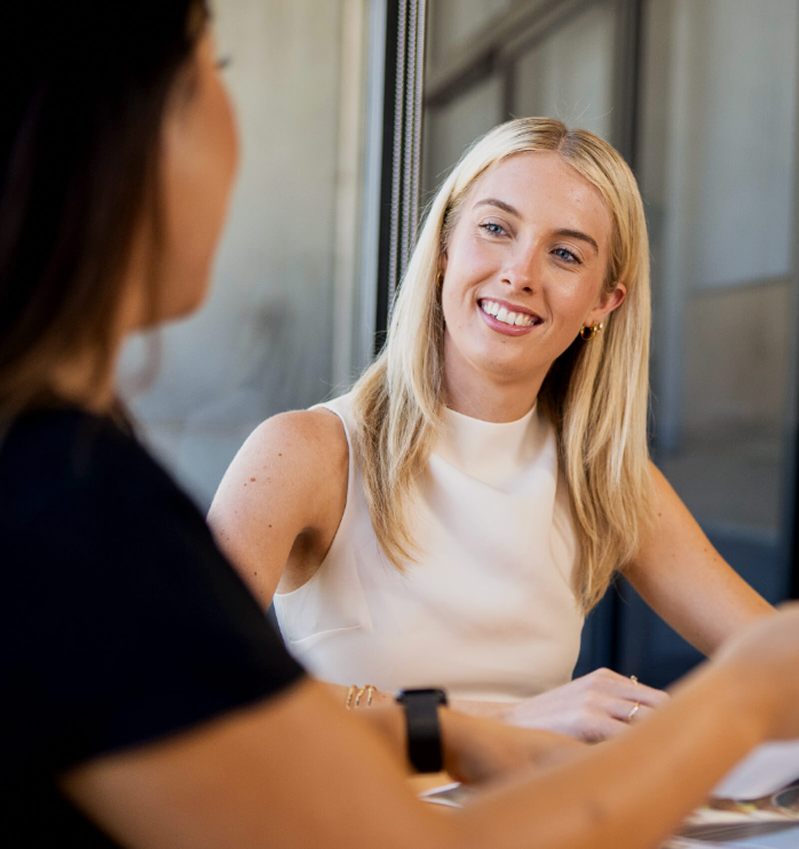 Realm team are seated at a table, engaging in conversation. One woman, with long blonde hair, is smiling and wearing a white top.