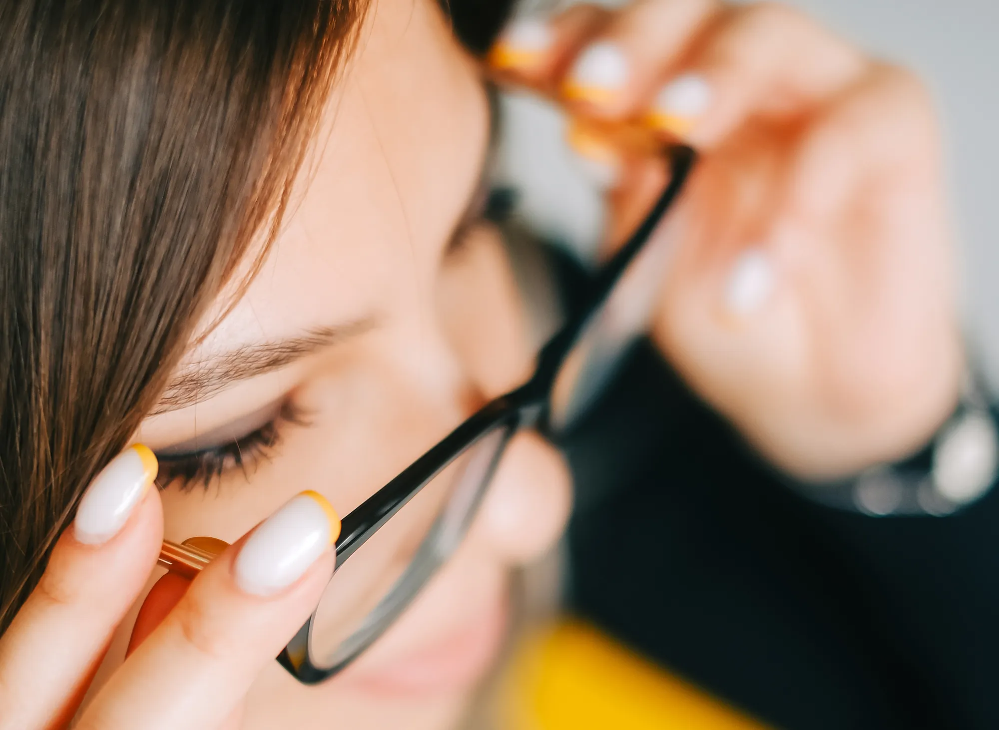 Close-up of a woman adjusting her black eyeglasses with yellow-accented nails.