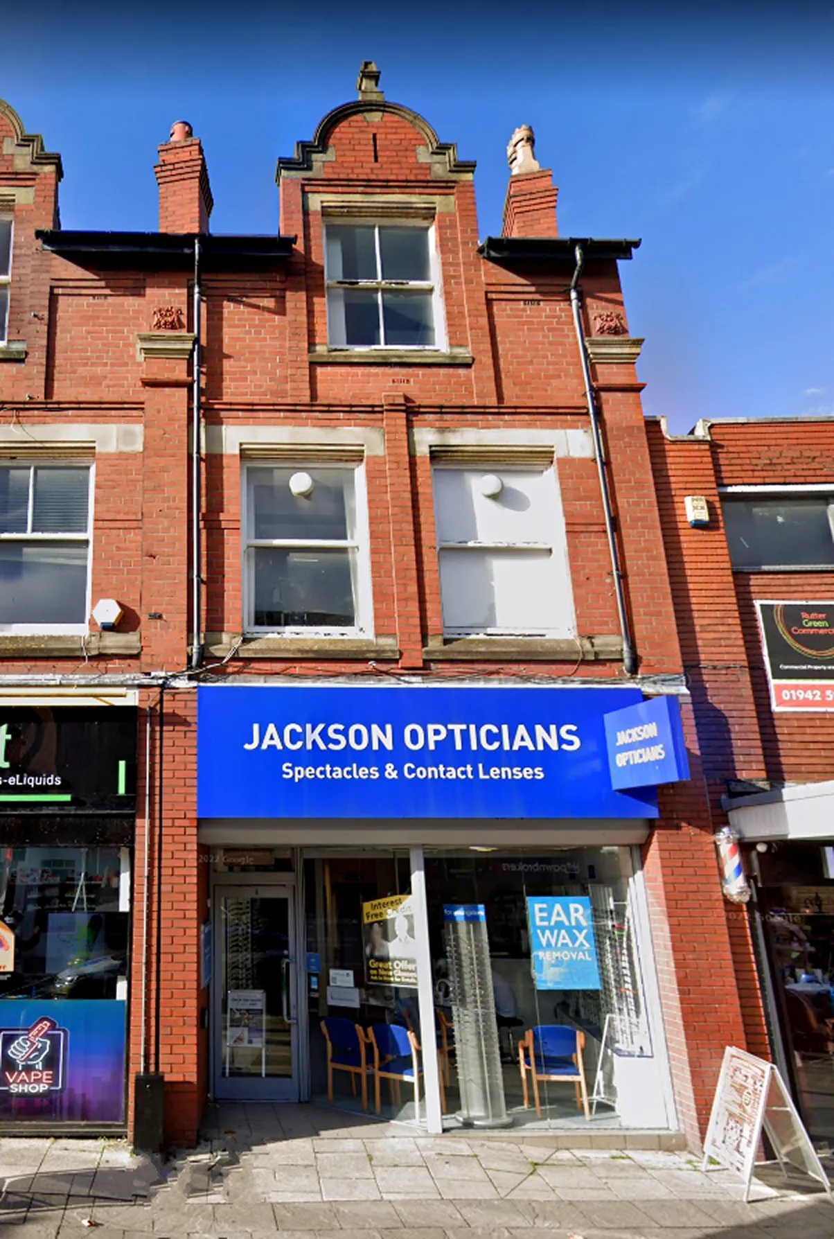 Jackson Opticians storefront with blue sign, brick building, chairs and promotional posters in windows.