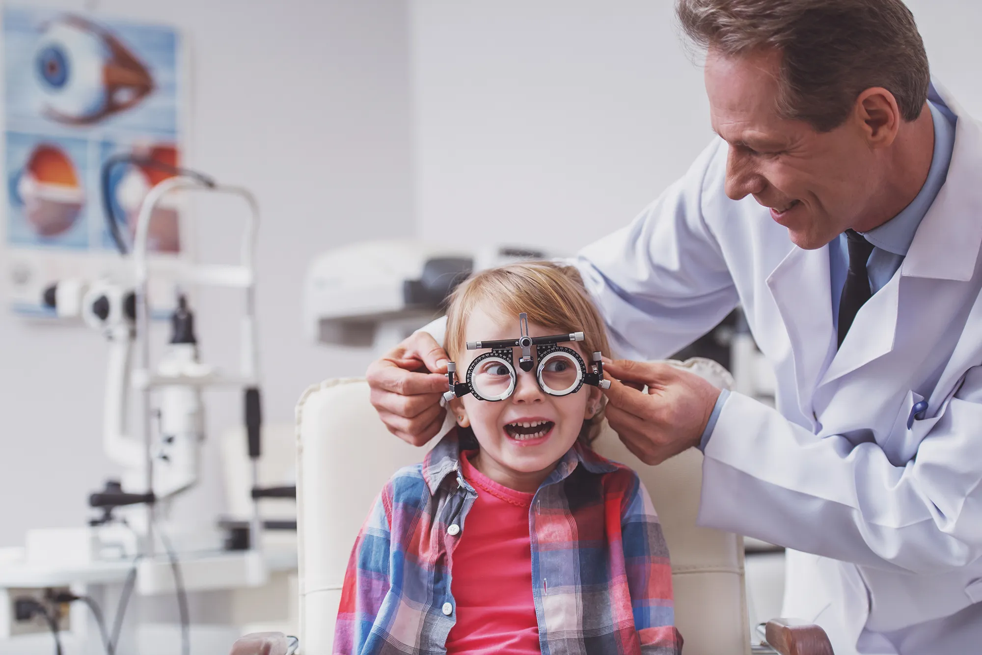 Optometrist fitting a young girl with a trial frame for an eye exam in a clinic.