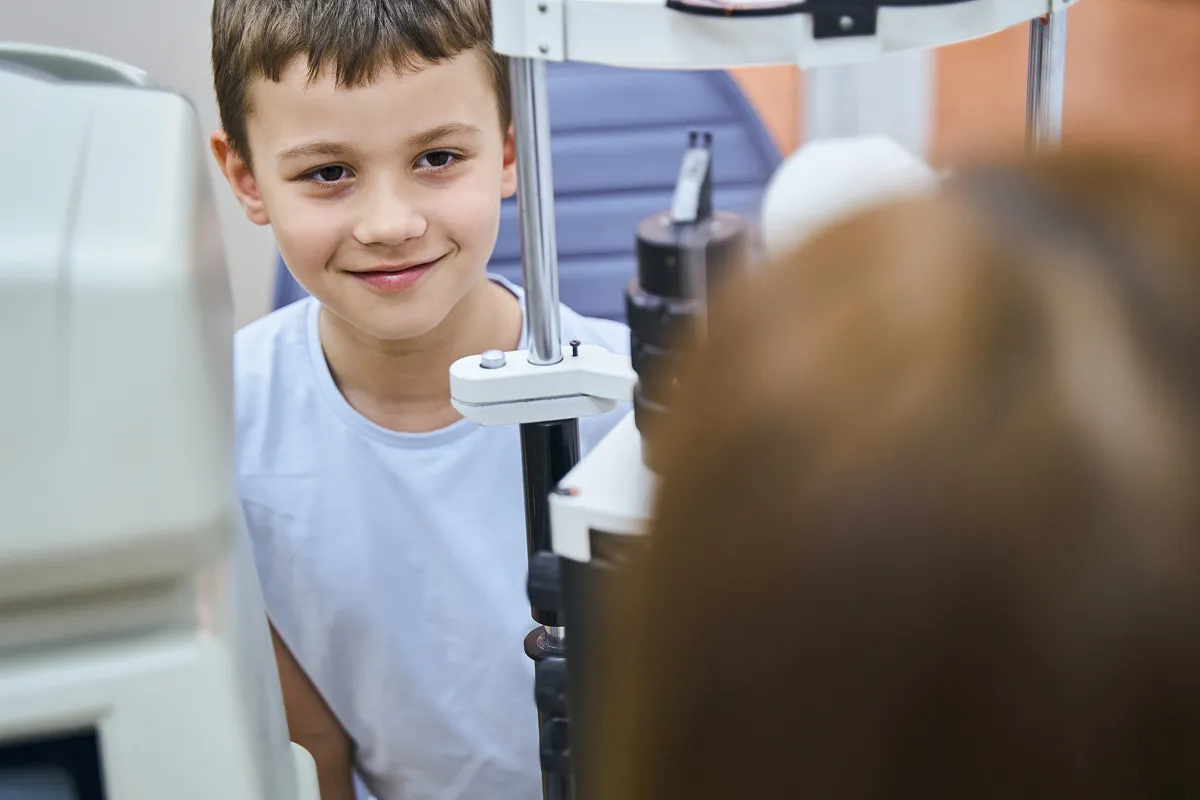 Young boy smiling while undergoing an eye examination with a slit lamp.