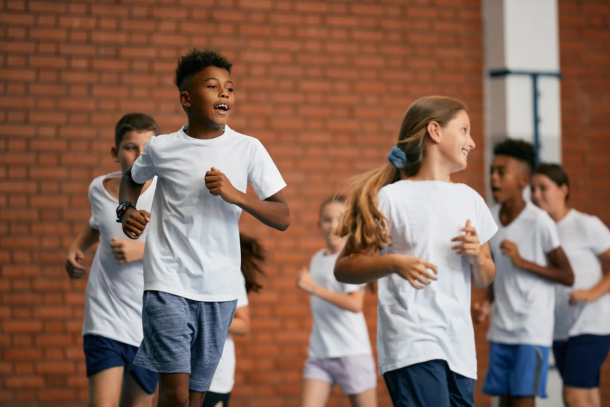Group of children running and exercising indoors against a brick wall background.