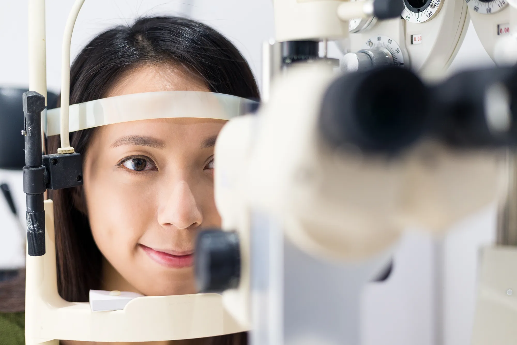 Woman undergoing an eye exam using a slit lamp device in an optometrist's office.