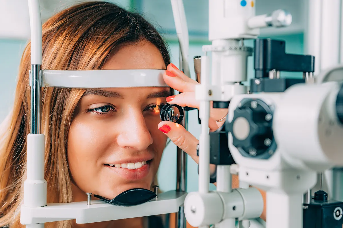 Young woman undergoing an eye exam using a slit lamp device at an optometrist's office.