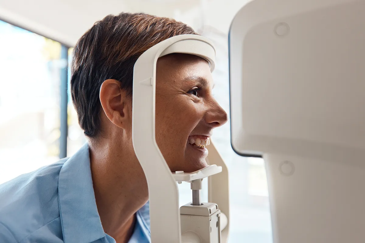 Smiling woman undergoing an eye examination using an optical machine.