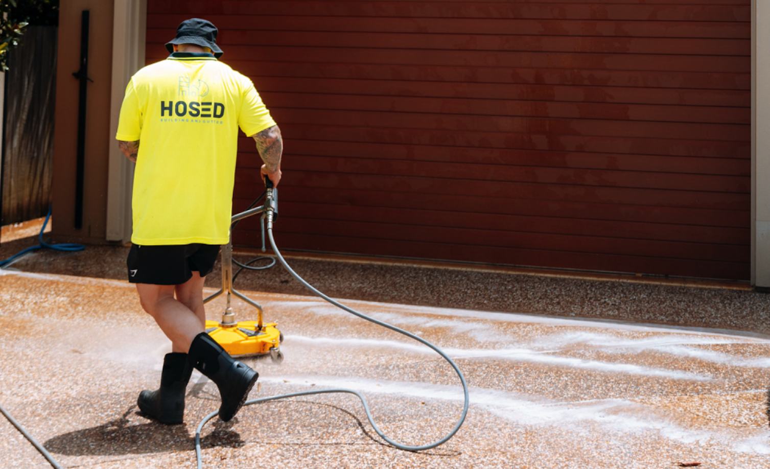 Technician with Hosed branded shirt pressure cleaning an exposed aggregate driveway.