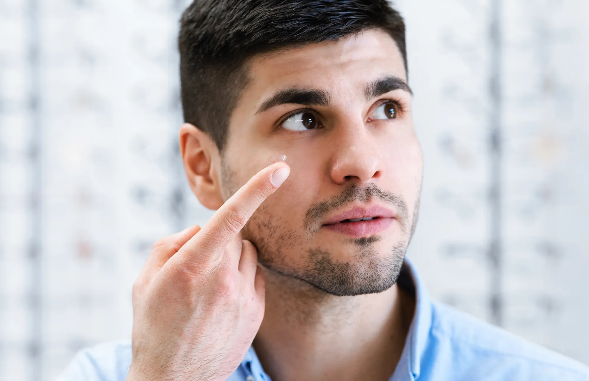 Young man holding a contact lens on his finger near his eye.