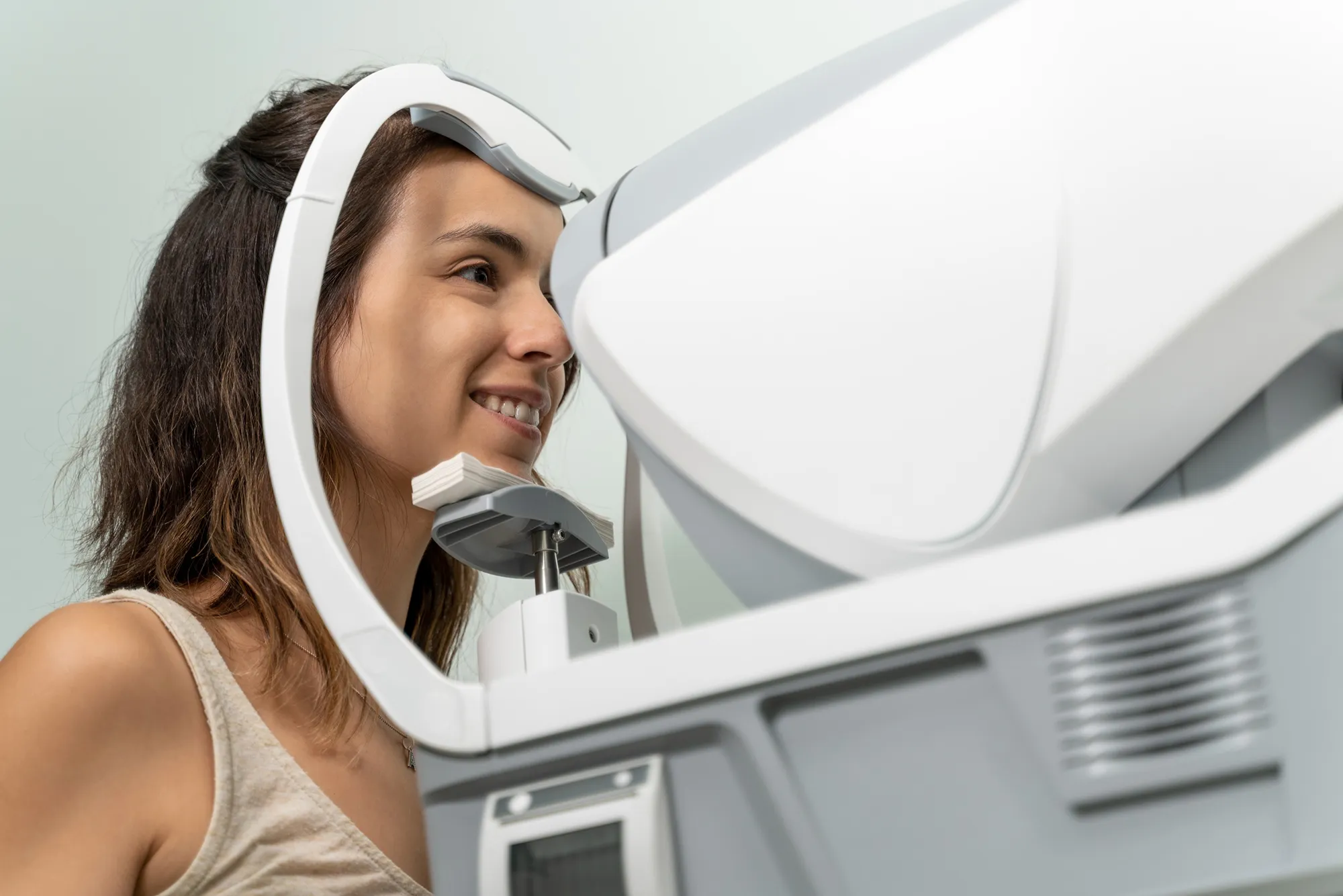 Woman undergoing an eye exam using a white autorefractor machine.