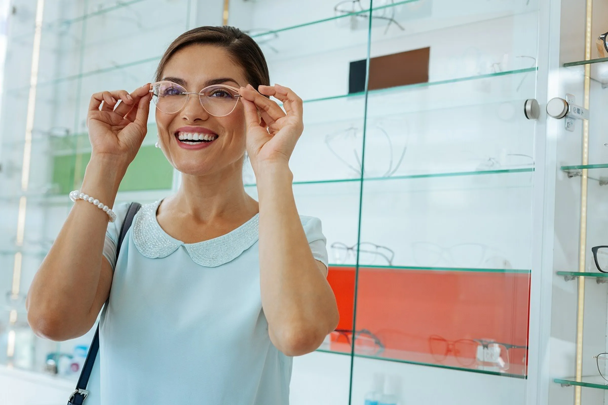 Smiling woman trying on clear eyeglasses in an optical store.