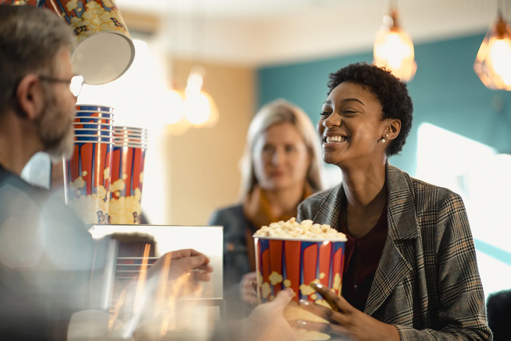 Smiling woman receiving a large popcorn bucket from a concession worker at a movie theater counter.