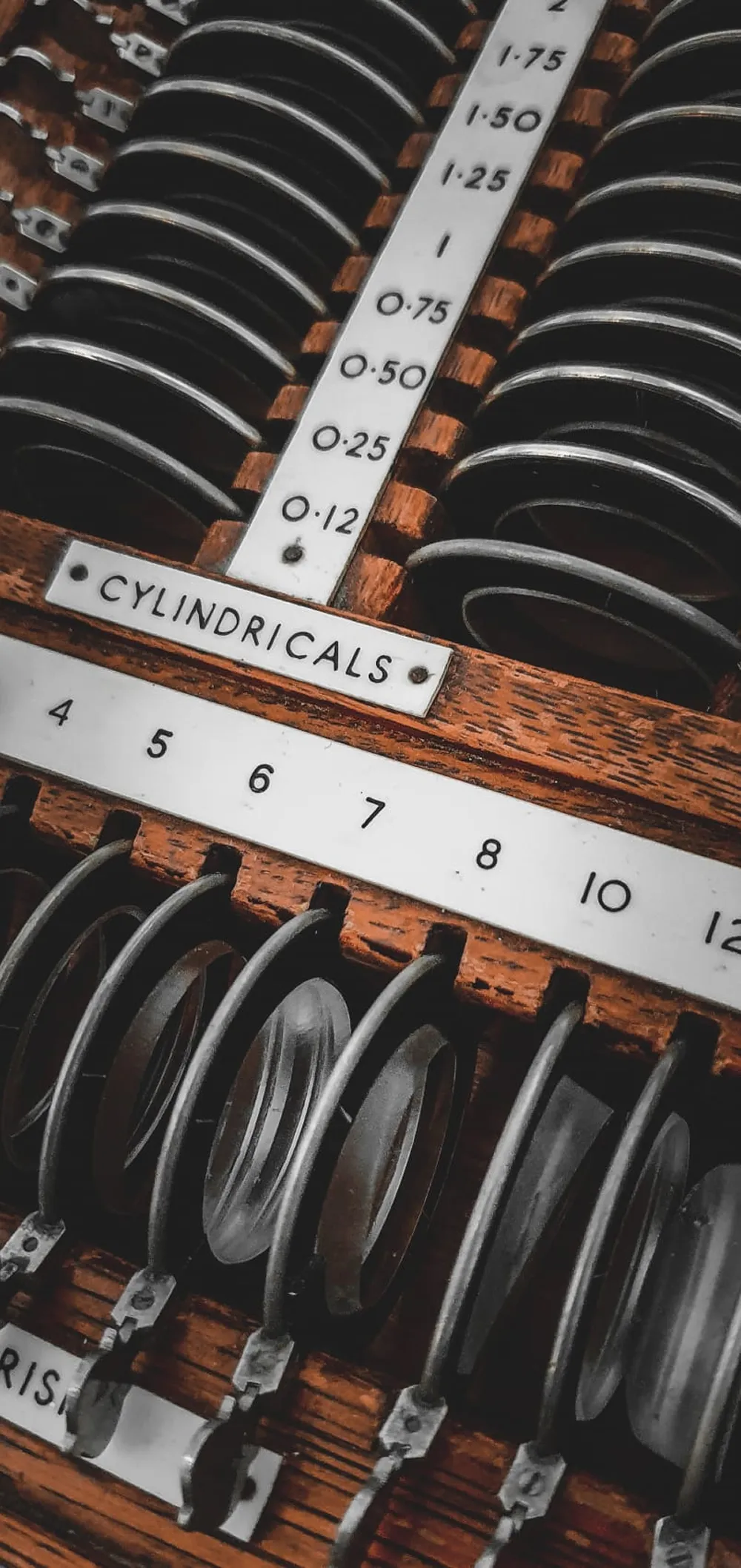 Wooden case with cylindrical lenses and a scale of measurements labeled cylindricals.