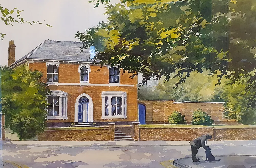 A brick house with white trim under trees; a person pets a black dog on a sidewalk corner.