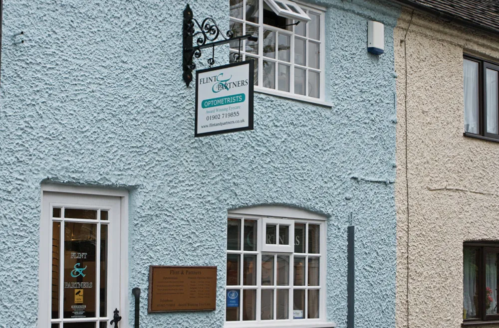 Blue stucco building with Flint & Partners optometrists signs and white framed windows and door.